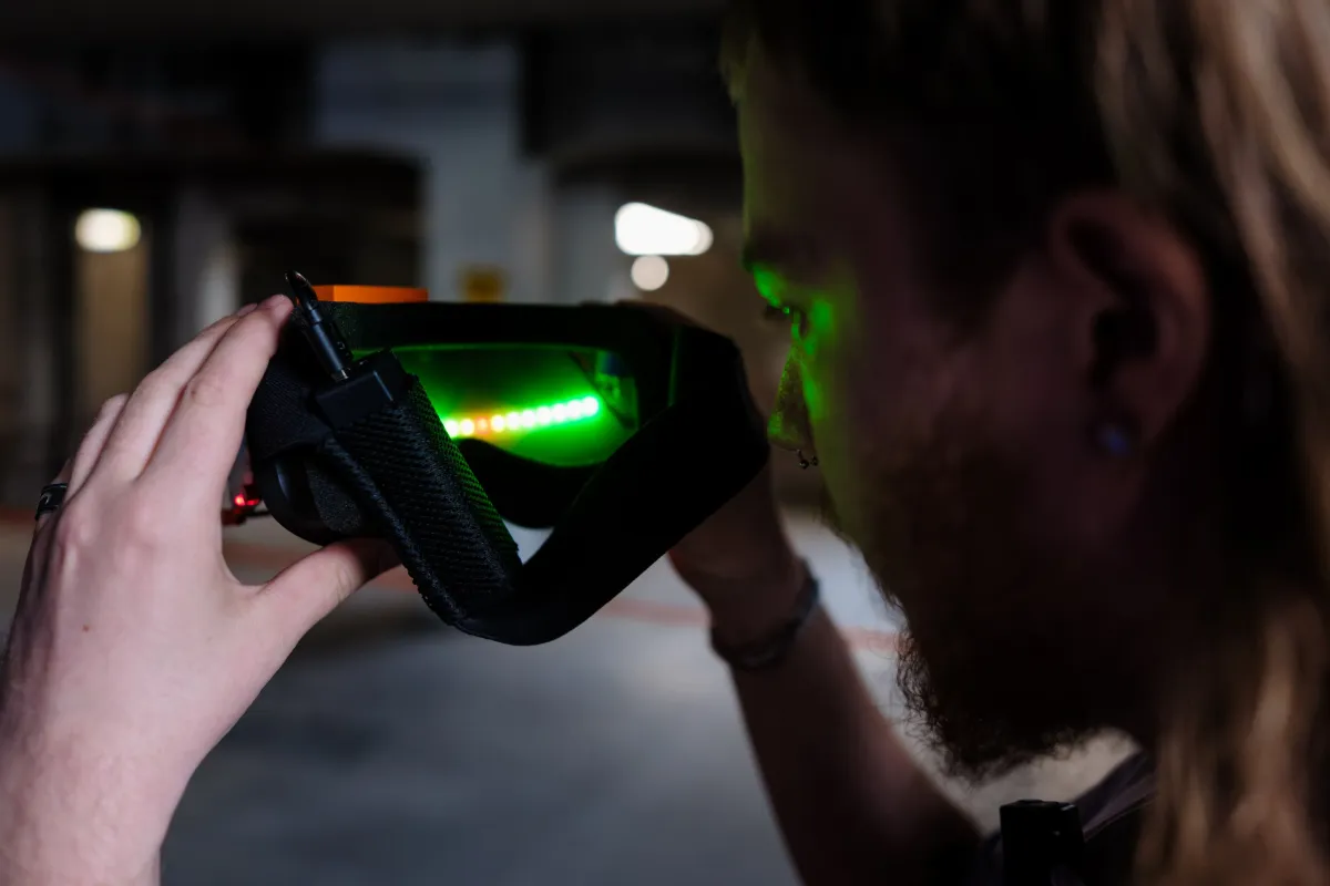 Niels Nicola looking at the inside of his radar goggles and holding them with both hands, while green light emits from them.